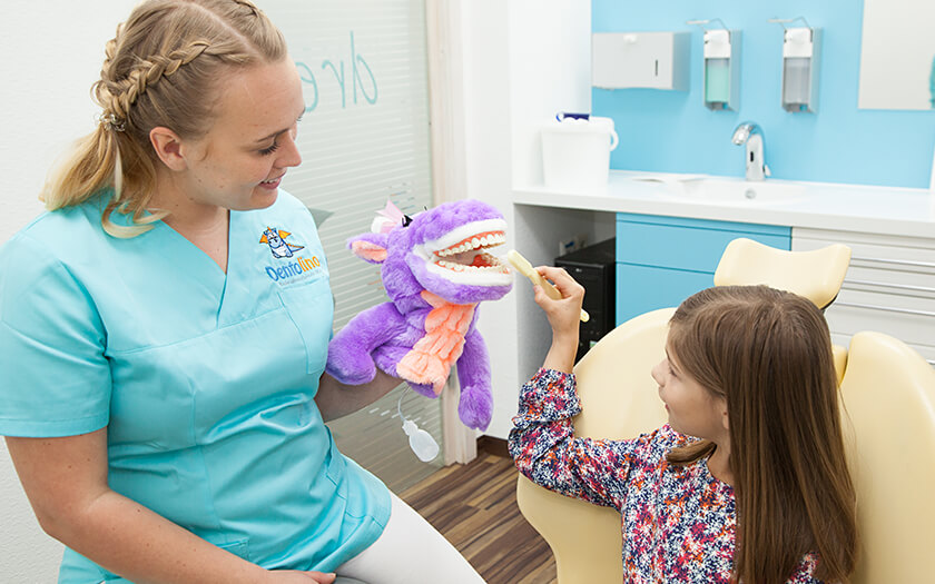 Zahnarzthelferin bringt Mädchen das Zähneputzen spielerisch mit Puppe bei.
